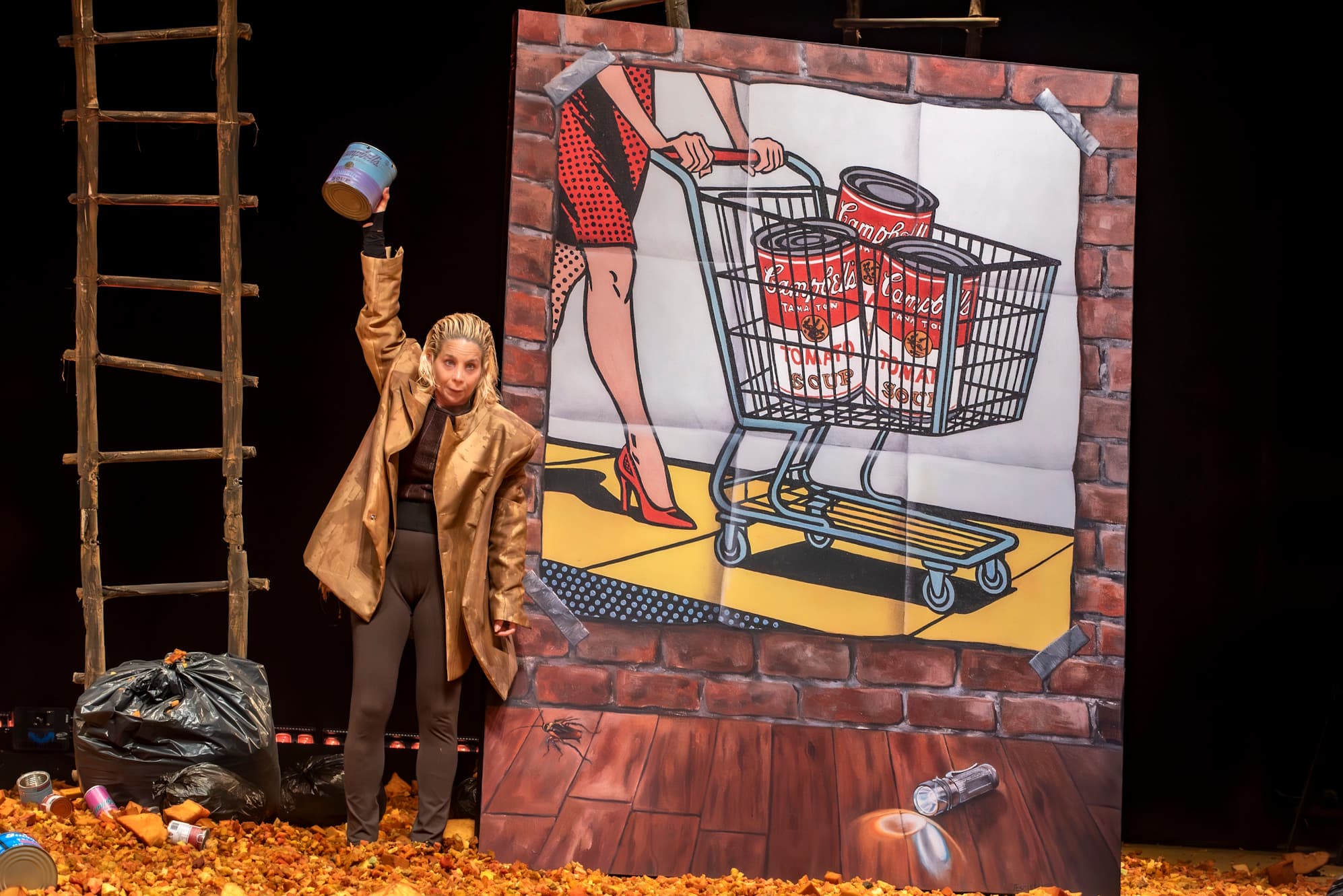 Cena de CHOQUE! com painel pop-art e elementos de consumo/lixo.