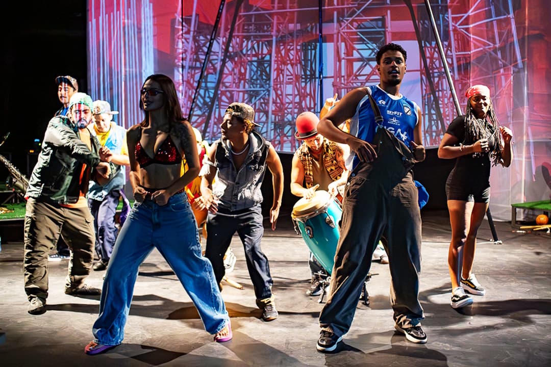 Cena de conjunto: performers em movimento, música e dança em cena.